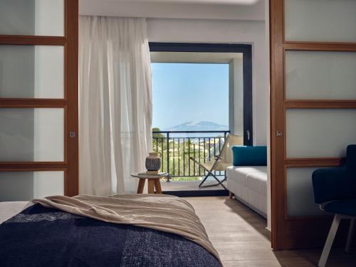 a bedroom with a bed and a view of a balcony at Cavo Orient Beach Hotel & Suites in Tragaki