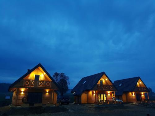 um grupo de três casas de madeira à noite em Osada Orlica 2 em Lasowka