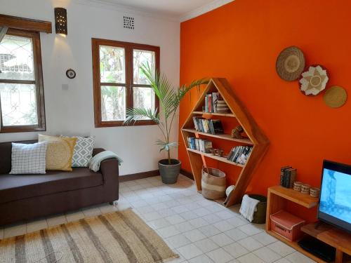 sala de estar con paredes de color naranja, sofá y TV en Utamaduni House B&B, en Arusha