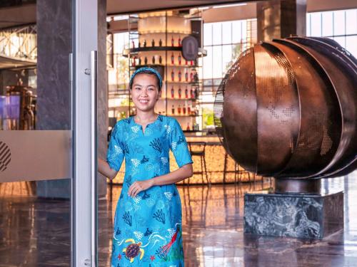 a woman in a blue dress standing next to a barrel at Pullman Phu Quoc Beach Resort in Phu Quoc