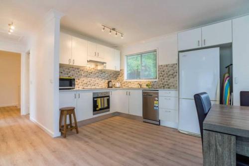 a kitchen with white cabinets and a wooden floor at Central Coast Escape in Point Clare