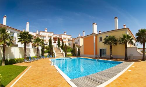 a swimming pool in front of a building with palm trees at The Village – Praia D’El Rey Golf & Beach Resort in Casal da Lagoa Seca