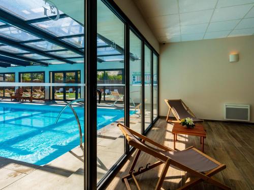 a swimming pool with two chairs in a room with windows at Garrigae Manoir de Beauvoir Poitiers Sud - Hotel & Spa in Mignaloux-Beauvoir