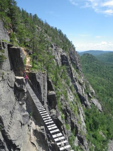 a person climbing up a mountain with a staircase on a cliff at Maison Accueillante - Spa, fleuve et montagnes! in Petite-Rivière-Saint-François