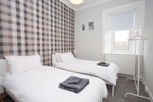 two beds in a room with a checked wall at The Warwick Apartment in Greenock