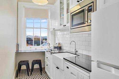 a white kitchen with a sink and two stools at Cromwell Apartment - 3 Red Doors Battery Point in Hobart