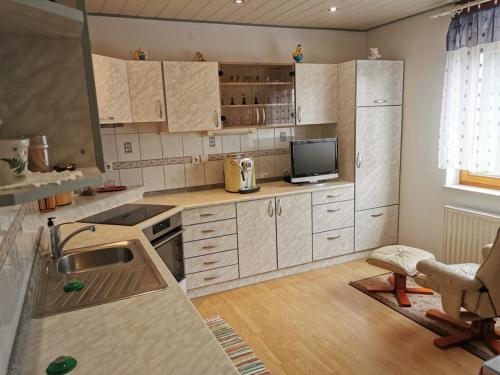 a kitchen with white cabinets and a sink and a tv at Urlaub für die Seele - Erholung Pur in der Natur - Ferienhaus mit Infrarotkabine & RELAX-Raum in Rucmanci