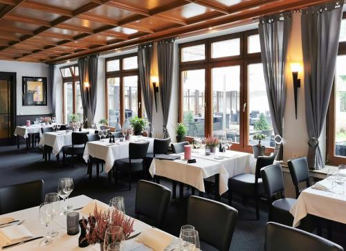 un ristorante con tavoli e sedie bianchi e finestre di Heidehotel Soltauer Hof a Soltau