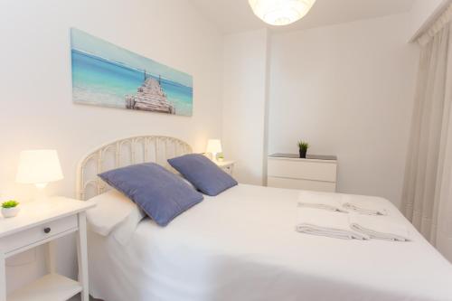 a white bed with two blue pillows in a bedroom at Los Olivos Apartment Cullera in Cullera