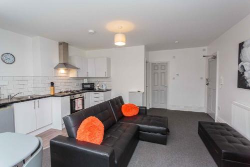 a living room with a black leather couch and orange pillows at Cherry Property - Orange Suite in Blackpool
