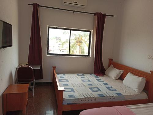 Schlafzimmer mit einem Bett, einem Fenster und einem Schreibtisch in der Unterkunft Hotel Saint-Jean in Cotonou