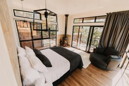 a bedroom with a bed and a chair and windows at Rainforest Gardens - Luxury Hillside Accomodation with Views to Bay & Islands in Mount Cotton
