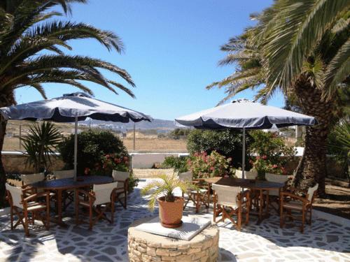 a patio with tables and chairs with umbrellas and palm trees at Villa Maria Vekri in Koufonisia