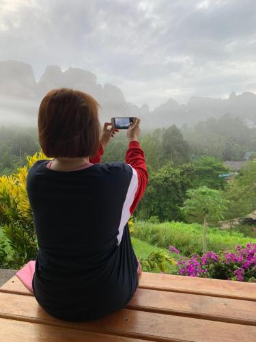 a woman taking a picture of the mountains with her cell phone at Billion Views Khaosok Homestay in Khao Sok