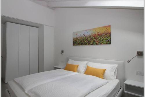 uma cama branca com almofadas amarelas e uma pintura na parede em La mansarda di Rossella em Pieve di Ledro