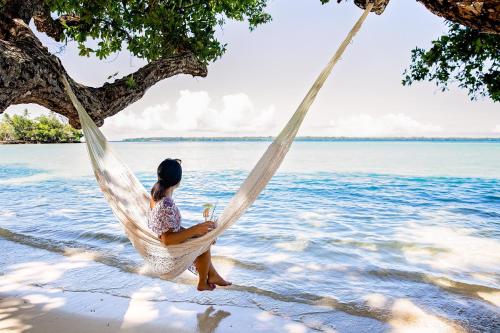 Barrier Beach Resort في لوجنفيل: امرأة تجلس على أرجوحة على الشاطئ