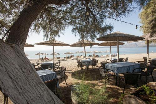 a beach with tables and chairs and umbrellas at Panagiota Apartments in Mavrovoúnion