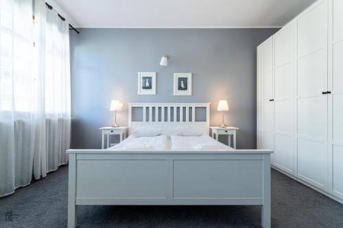 a white bedroom with a white bed and two tables at Victus Apartamenty, Apartament Lighthouse in Gdańsk