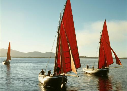 three boats with red sails in the water at Cnocan Na Cuaig Carraroe by Trident Holiday Homes in Carraroe