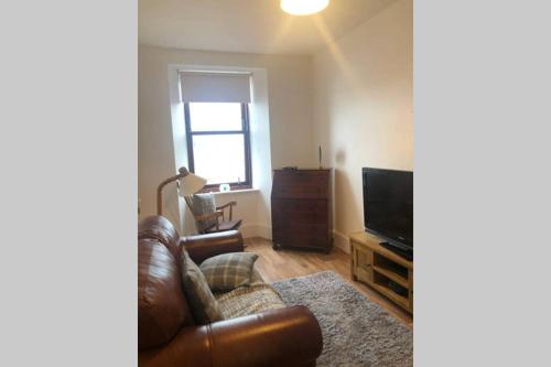 a living room with a leather couch and a television at Centrally located 1 bed modern flat with harbour views in Wick