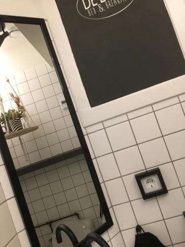 a mirror in a bathroom with a white tiled wall at B&B de Loeff in Waalwijk