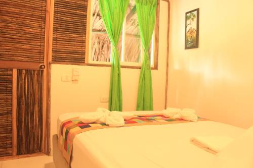 a bed in a room with green curtains and a window at La Natura Hostel & Pool in Palomino
