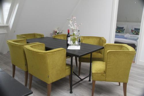 a dining room table with yellow chairs and a bottle of wine at Bed & Breakfast Geesberge in Maarssen