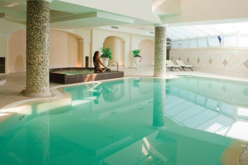 a woman sitting in a swimming pool in a building at Sant Alphio Garden Hotel & SPA in Giardini Naxos