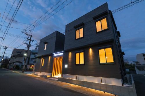 una casa negra con ventanas iluminadas en una calle en J-STAY Beppu indigo, en Beppu