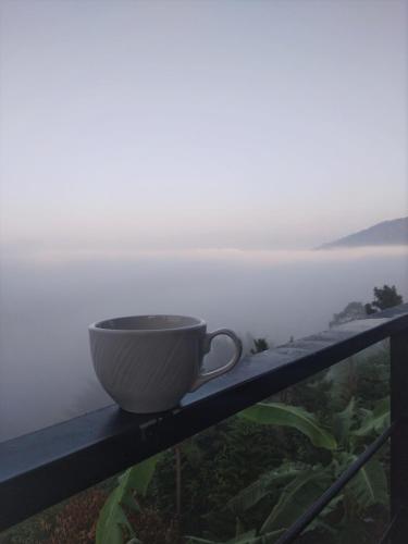 a coffee cup sitting on a ledge overlooking the ocean at ภูน้ำทิพย์ รีสอร์ท in Ban Huai Phai