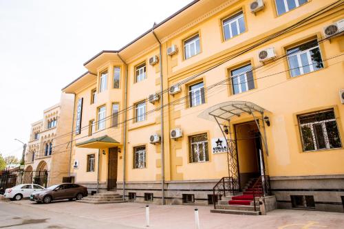 een geel gebouw met auto's ervoor geparkeerd bij Stella Hotel Tashkent in Tasjkent