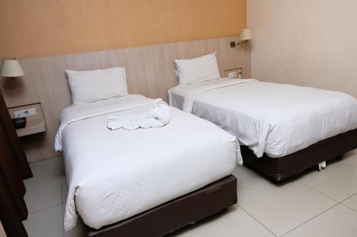 two beds with white sheets and a stuffed animal on them at Rio City Hotel in Palembang
