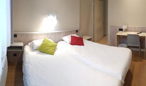 a white bed with four colorful pillows on it at Hôtel La Bérangère in Pérouges