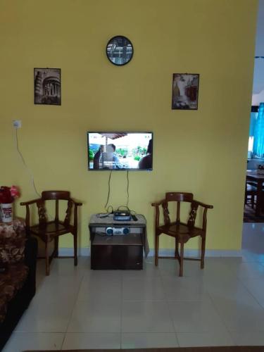 ein Wohnzimmer mit 2 Stühlen und einem TV an der Wand in der Unterkunft Cik Kerinting Homestay in Jitra