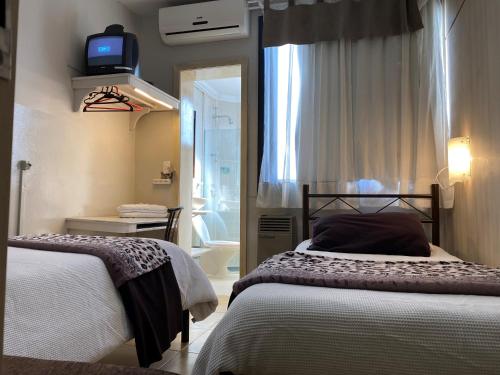 a bedroom with two beds and a tv on the wall at Pousada Thiany in Bento Gonçalves