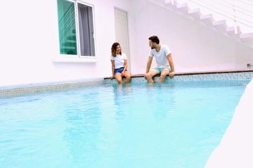 a man and woman sitting on the edge of a swimming pool at Casa Gem B&B in Playa del Carmen