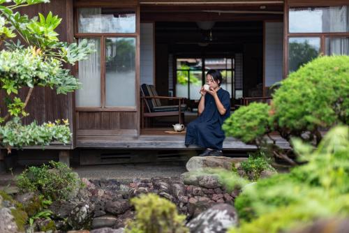 a woman talking on a cell phone in front of a house at Hostel 東風ノ家（Kochi-no-ya） in Aki