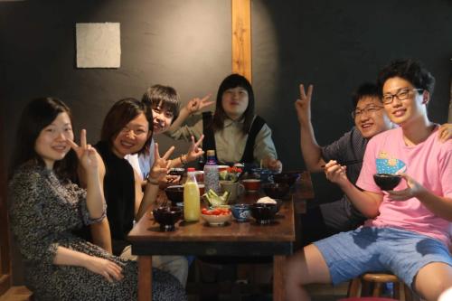 a group of people sitting at a table with their hands up at Hostel 東風ノ家（Kochi-no-ya） in Aki
