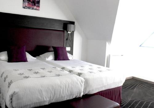 a bedroom with a large white bed with purple pillows at The Originals City Hôtel, Aéroport Beauvais in Beauvais