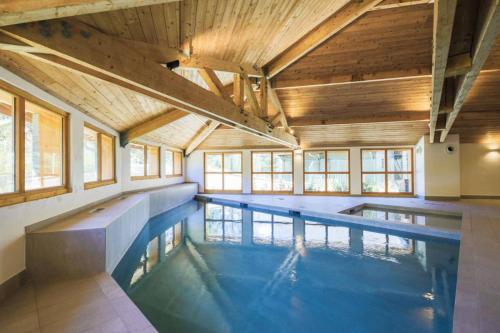 une grande piscine intérieure avec des plafonds en bois et des fenêtres. dans l'établissement Residence Les Melezes - maeva Home, à La Joue du Loup