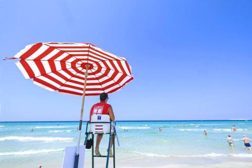 a man standing on a lifeguard stand under an umbrella on the beach at Ecoresort Le Sirene - Caroli Hotels in Gallipoli