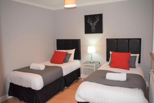 two beds in a room with red and white at Kelpies Serviced Apartments- Campbell in Pumpherston
