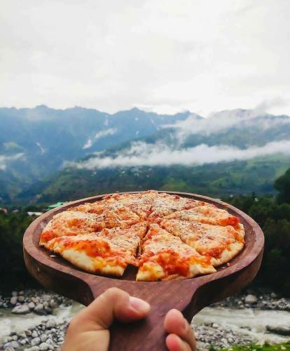 una persona sosteniendo una pizza en una tabla de cortar en 8fold by Larisa, Jibhi, en Jibhi