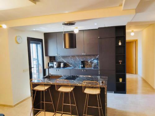 Luxueux appartement entre Gueliz et l'Hivernage avec WIFI في مراكش: مطبخ مع خزائن سوداء وكراسي البار