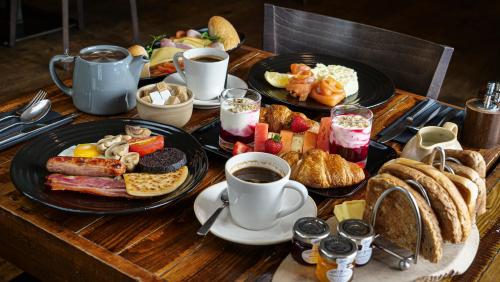 a wooden table topped with plates of breakfast foods and coffee at Bosville Hotel in Portree