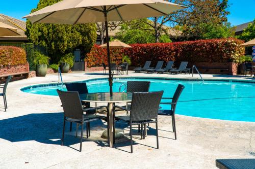 a table with chairs and an umbrella next to a pool at Hotel Piccadilly in Fresno