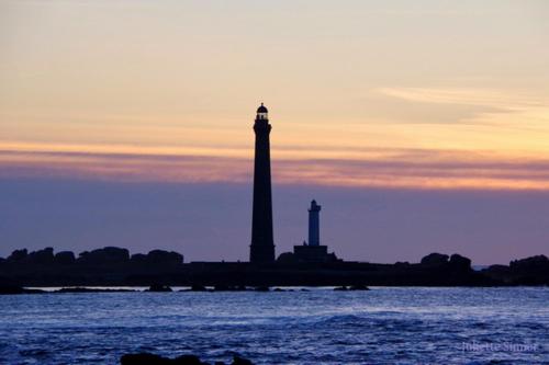 a lighthouse on an island in the water at sunset at Maison Molène, au Pays des Abers Plouguerneau in Plouguerneau