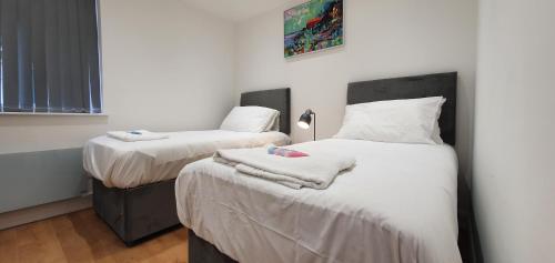 a bedroom with two beds with white sheets and towels at Garland Stylish Apartment 2 In Greater London in London