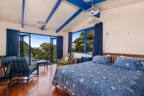 a bedroom with a bed and some chairs and windows at Pohutukawa Cottage - Matakana Holiday Home in Tawharanui
