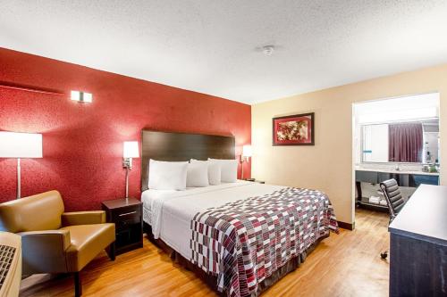 a hotel room with a bed and a chair at Red Roof Inn and Suites Battle Creek in Battle Creek